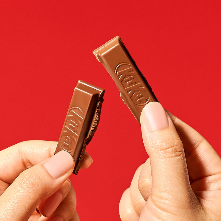 Two hands holding broken pieces of a Japanese Kit Kat: Chocolate & Ehime Iyokan Orange by Nestle Japan against a red background.