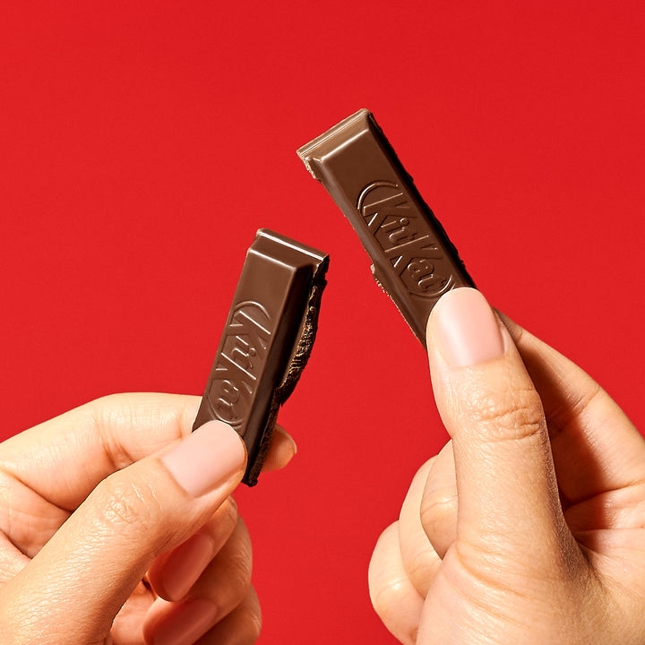 Two hands holding a snapped Nestle Japan Dark Chocolate Kit Kat bar against a red background.