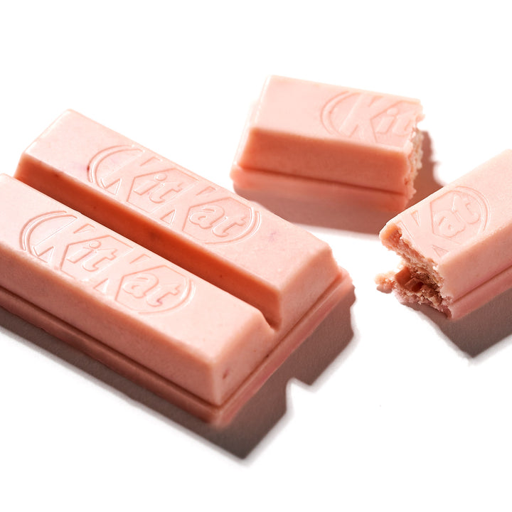Three bittersweet Strawberry Otona no Amasa Kit Kat bars with one piece partially bitten, isolated on a white background.