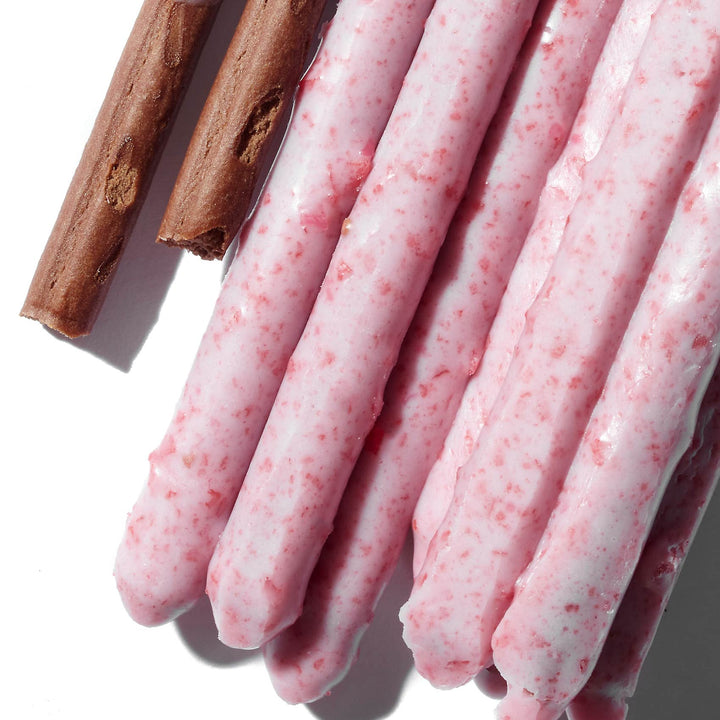Pink Glico Pocky: Variety Pack sticks with speckles, accompanied by two cinnamon sticks, on a white background.