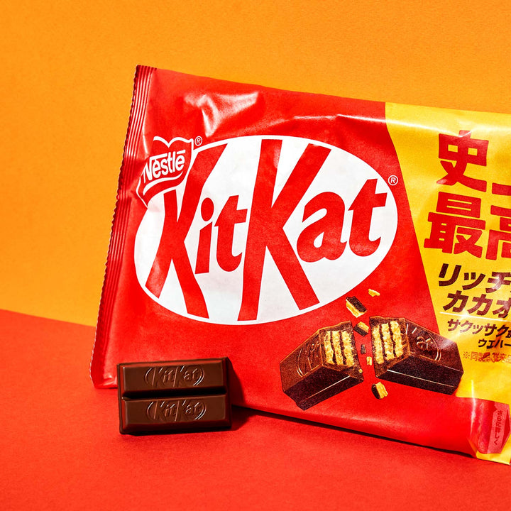 A bag of Nestle Japan Japanese Kit Kat: Original Chocolate with two chocolate pieces in front, against an orange background.