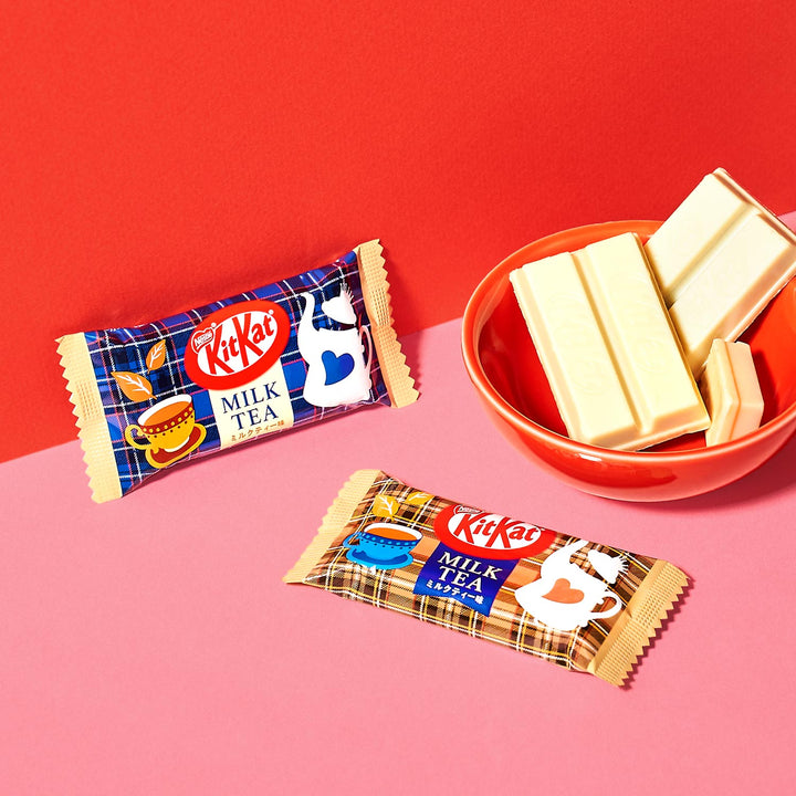 Two Nestle Japan Milk Tea Kit Kat flavor bars beside a bowl of white chocolate pieces on a red surface, contrasting with a pink background.