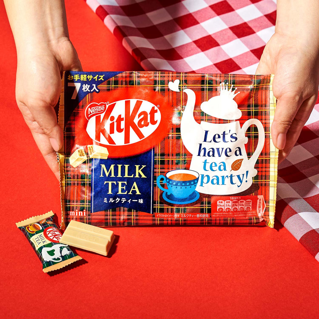 Hands holding a package of Nestlé Japan Milk Tea Kit Kat with the slogan "let's have a tea party!" and an open teabag on a red and white checkered cloth.