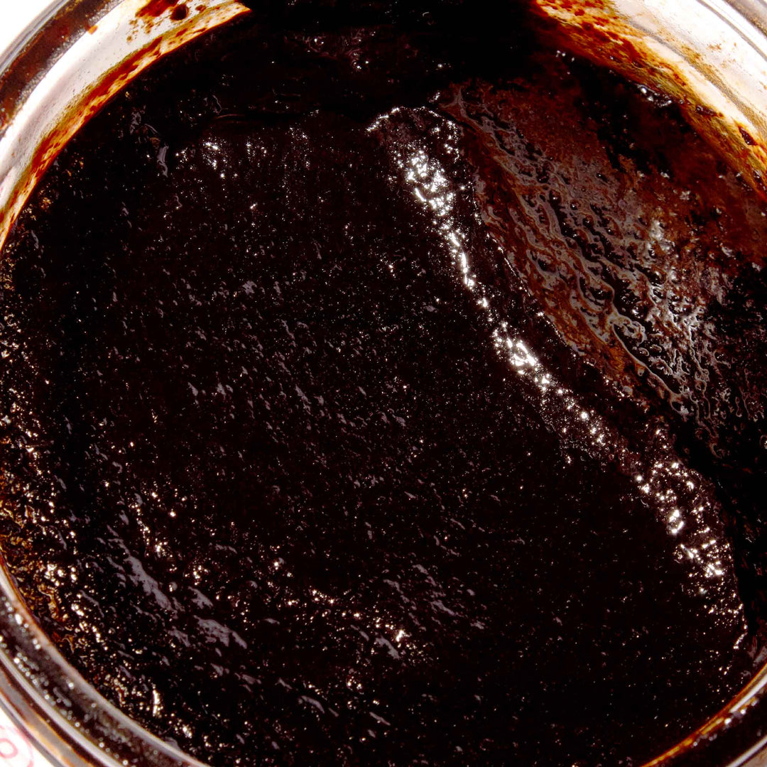 A jar of Assi Jjajang Black Bean Sauce with a spoon in it.