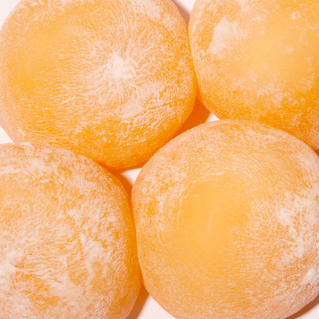 Close-up of Kubota Mikan Orange 4 Pack Daifuku Mochi ice cream with a dusting of powder on a white background.