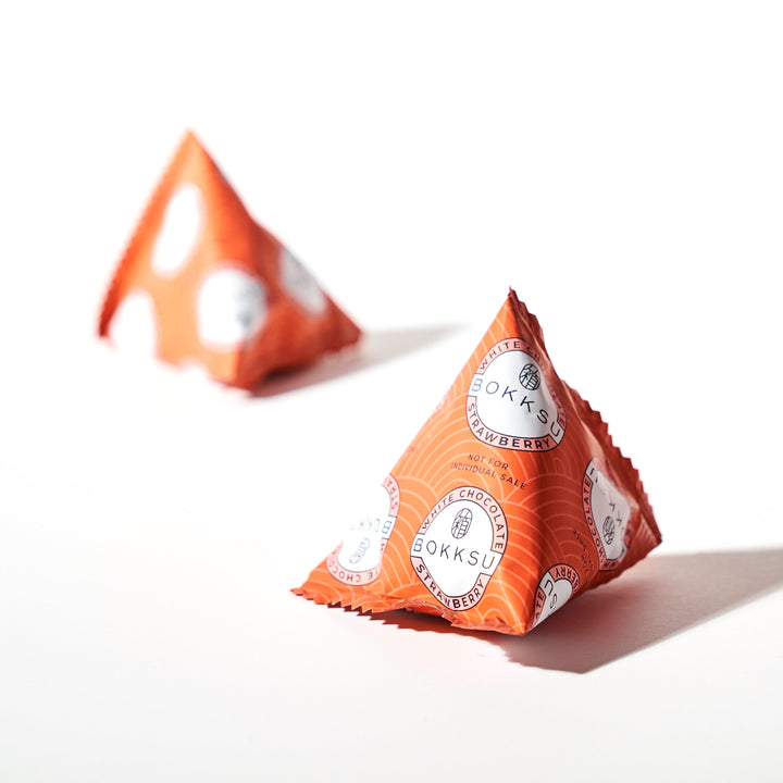 Two orange triangles on a white surface, reminiscent of a Bokksu White Strawberry 6-Piece Box by Bokksu.