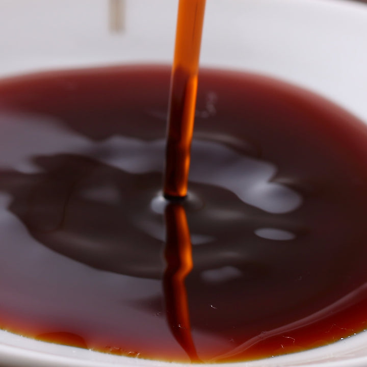 Kikkoman Soy Sauce with Dispenser Bottle is being poured from a dispenser bottle into a bowl, an essential table condiment.
