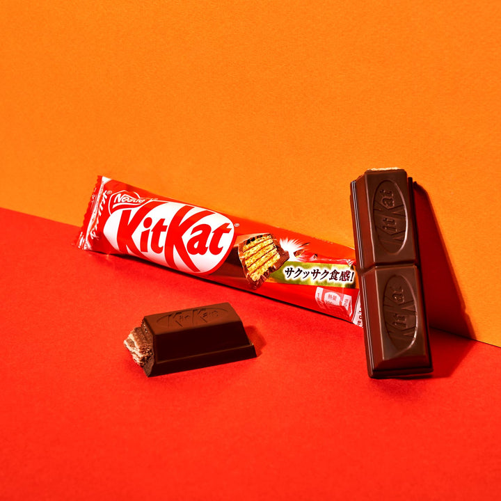 A Nestle Japan Japanese Kit Kat chocolate bar with original packaging beside an unwrapped bar showing two separated pieces on a red-orange background.