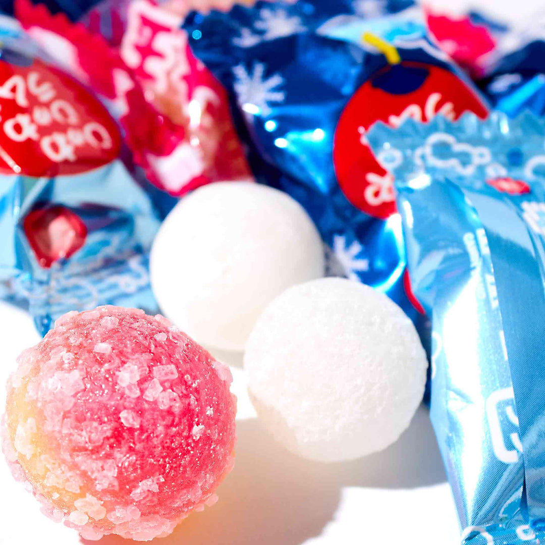 A group of Senjaku Cool & Bubbly Ramune Candy balls and Senjaku candy wrappers on a white surface.