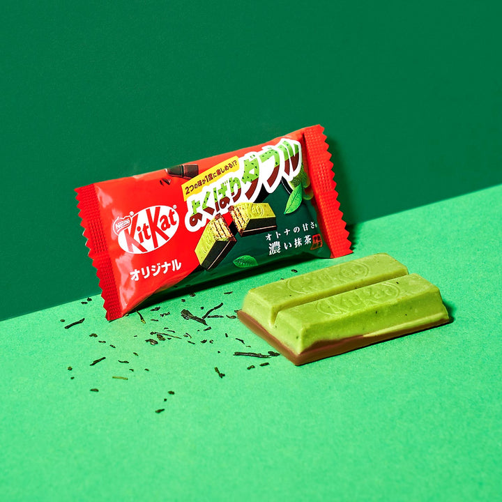 A Green Tea Double Layer Japanese Kit Kat bar by Nestle Japan with its packaging, partially unwrapped, exposing the chocolate on a green background.