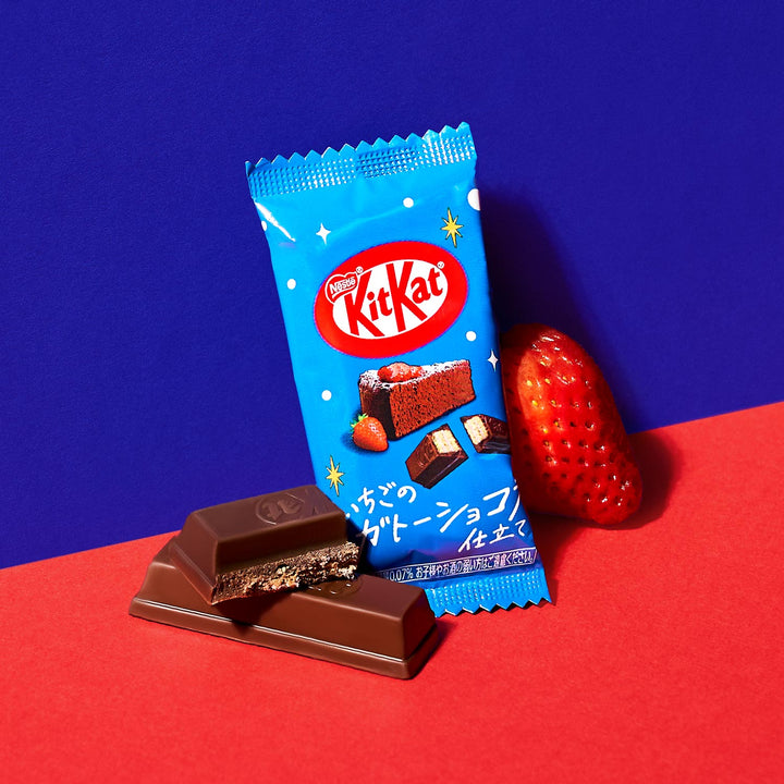 A package of Nestle Japan's Japanese Kit Kat: Strawberry Chocolate Cake with a partially unwrapped chocolate bar and a fresh strawberry on a blue and red background.