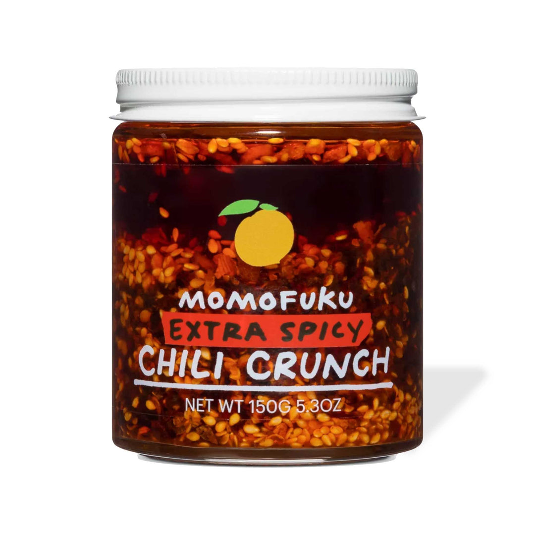 A jar of Momofuku Chili Crunch: Extra Spicy sauce, displaying abundant chili flakes and habanero peppers, against a white background.