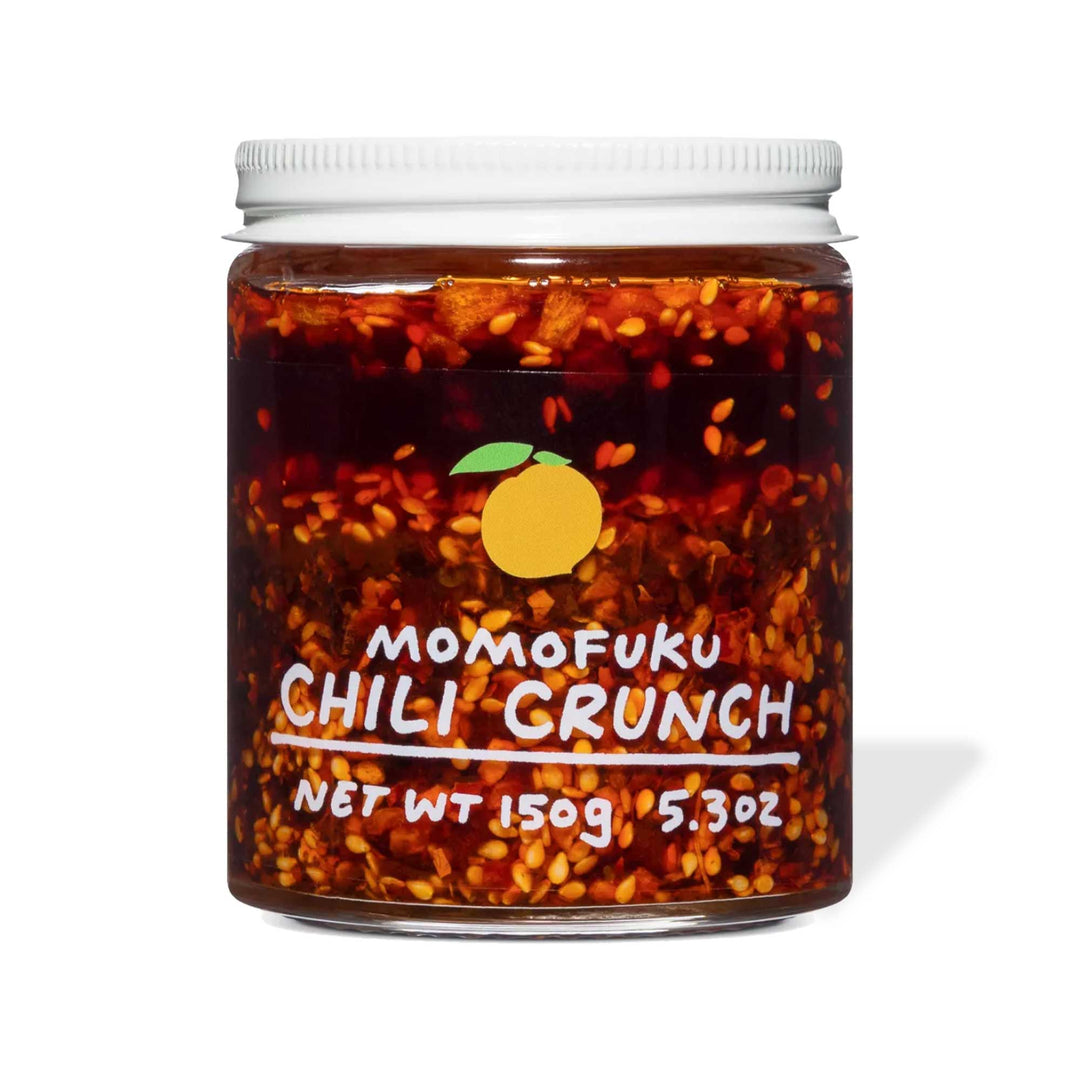 A jar of Original Momofuku Chili Crunch by Momofuku with red chili flakes visible, labeled with weight details, against a white background.