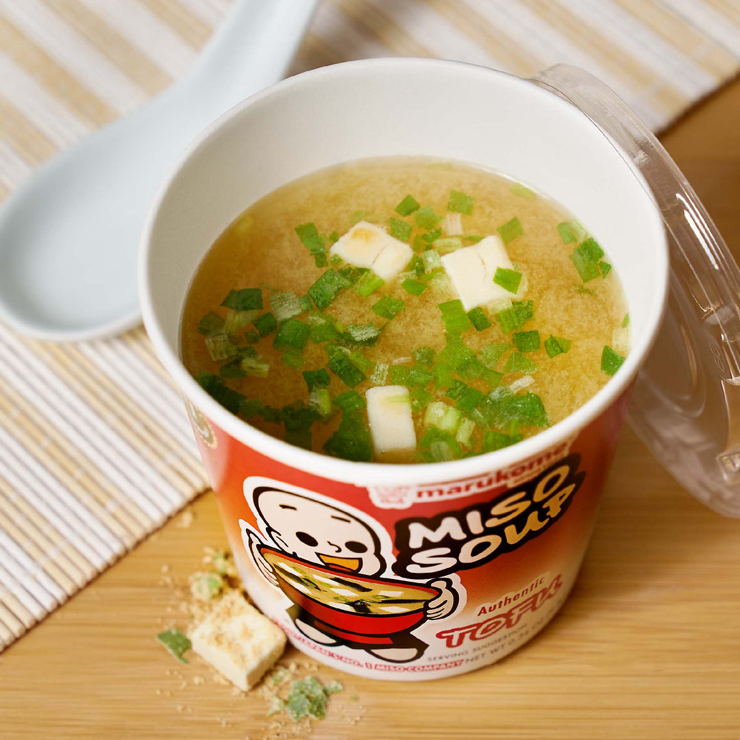 A Marukome Instant Miso Soup Cup: Tofu is sitting on top of a wooden table.
