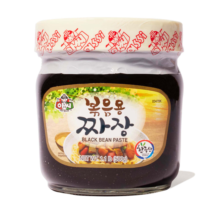 A jar of Assi Jjajang Black Bean Sauce on a white background.