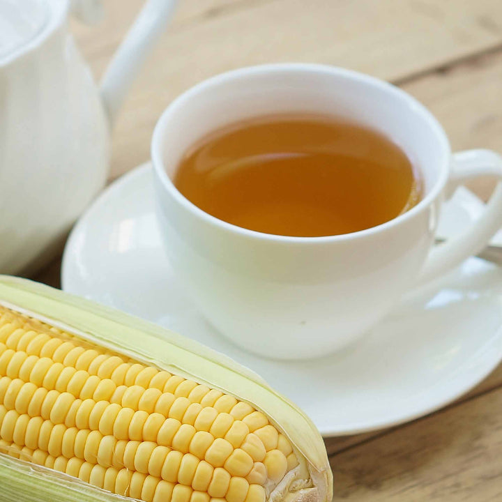 A cup of Surasang Organic Caffeine-Free Roasted Corn Tea (25 bags) and a cob of corn on a table.