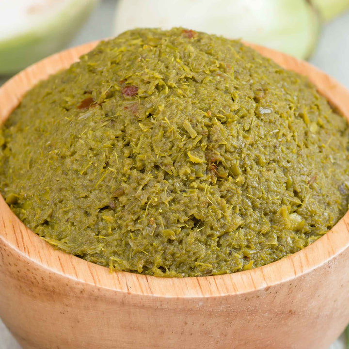 A bowl of Maesri Thai Green Curry Paste on a wooden table.