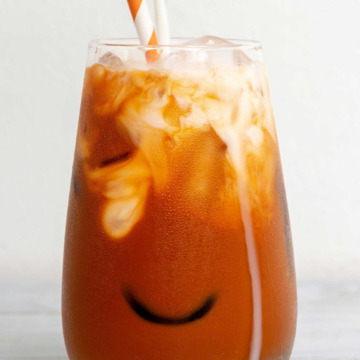 A glass of Ranong Tea 3-in-1 Instant Thai Tea Mix with a smiley face on it.