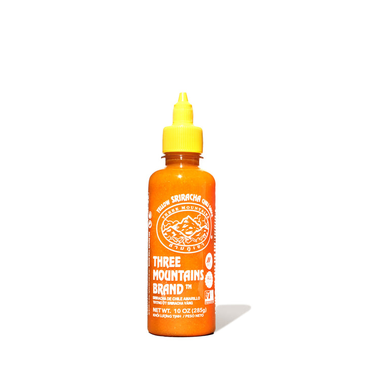 A bottle of Three Mountains Original Sriracha: Yellow sauce on a white background.