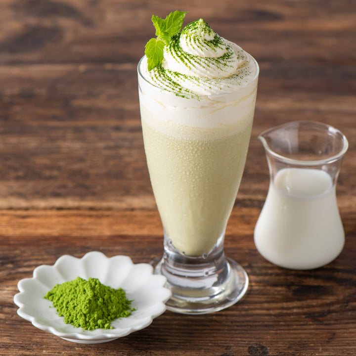 A Kuze Fuku Matcha Latte Mixer with whipped cream and milk on a wooden table.