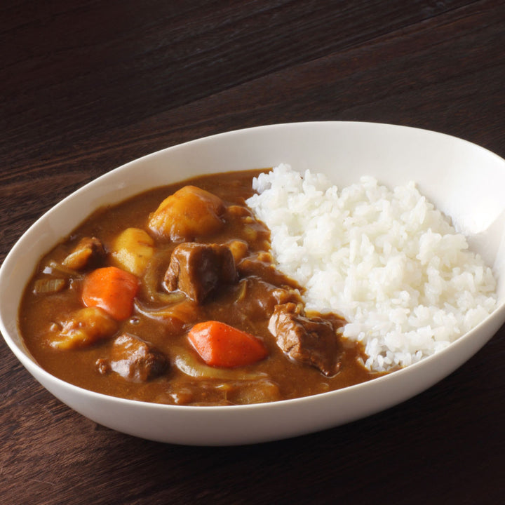 A bowl of hot, spicy House Curry Sauce with Vegetables and rice on a wooden table.