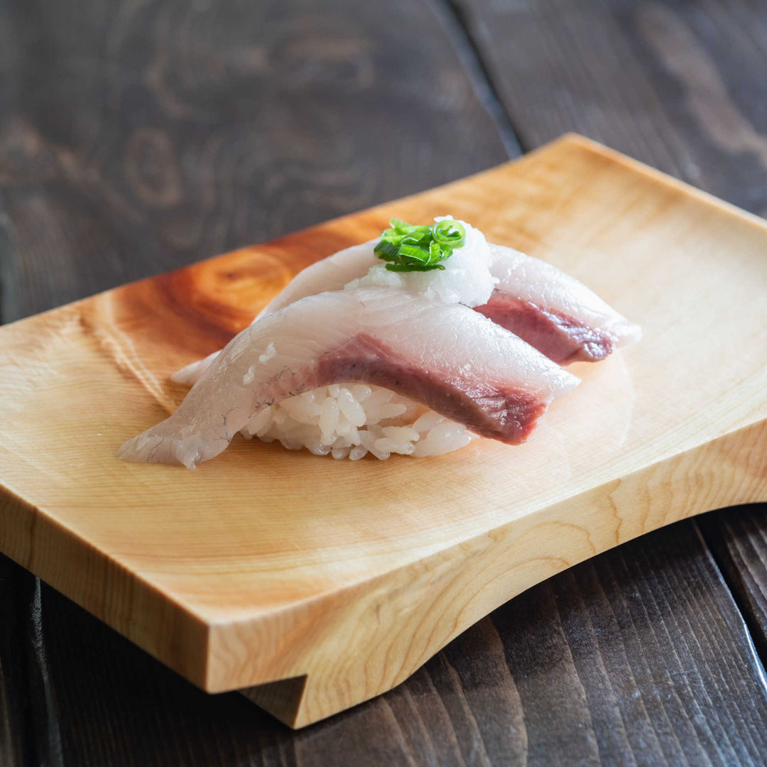 A piece of Sashimi-Grade Uogashi Yellowtail Hamachi Buri Loin (1 lb) is sitting on a wooden plate.