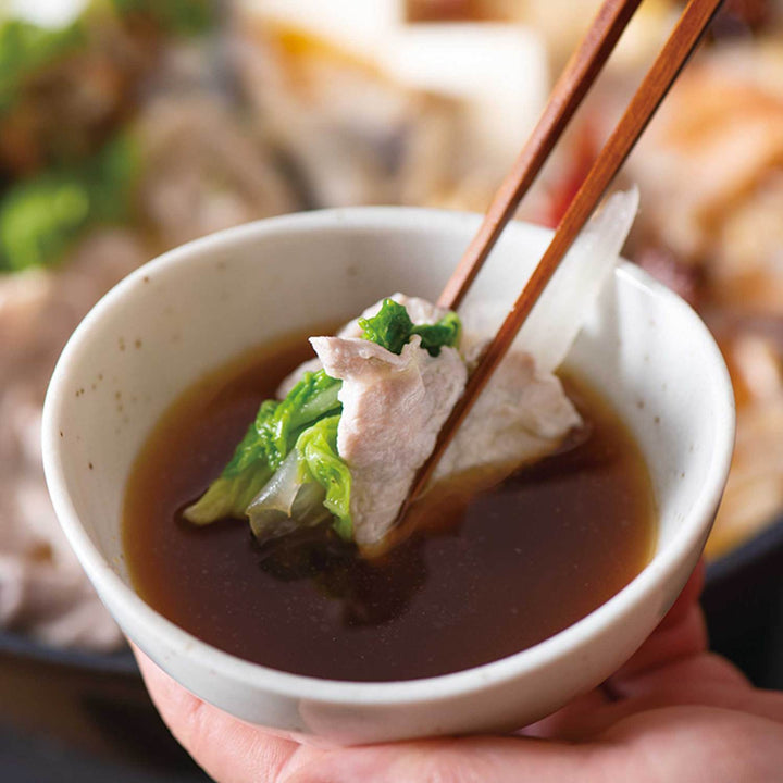 A person holding a bowl of soup with Kuze Fuku Premium Dashi Ponzu with Yuzu chopsticks.