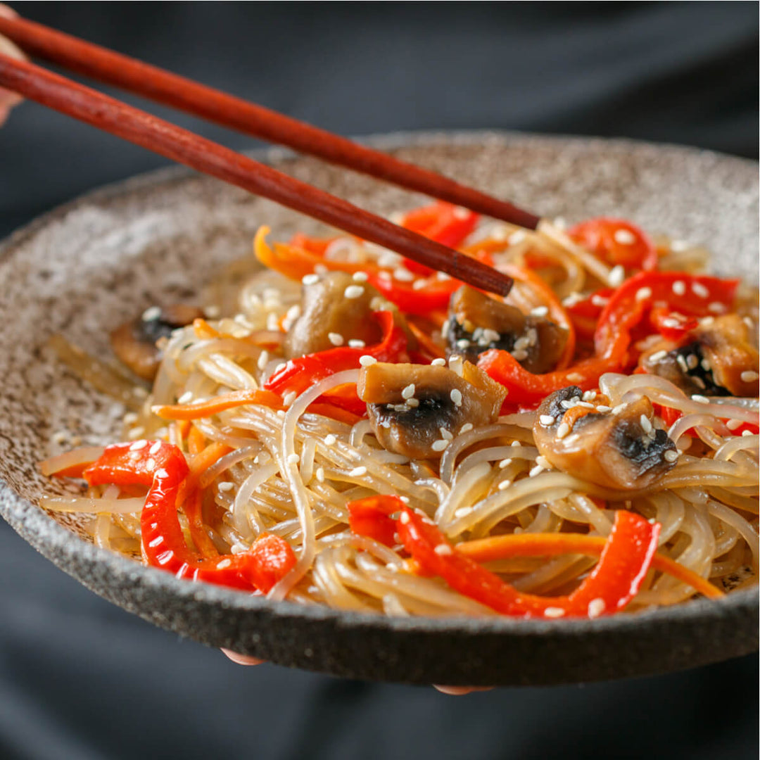 A person holding a Surasang Sweet Potato Starch Noodle bowl with mushrooms and peppers.
