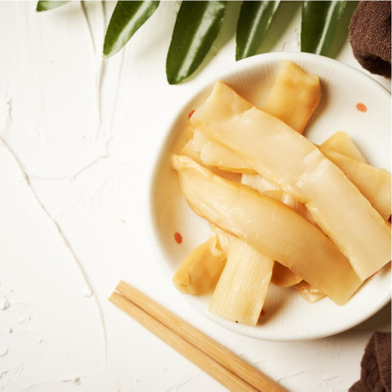 A bowl of Momoya Menma Pickled Bamboo Shoots on a white surface with chopsticks to the side, ready to be used as a ramen topping.