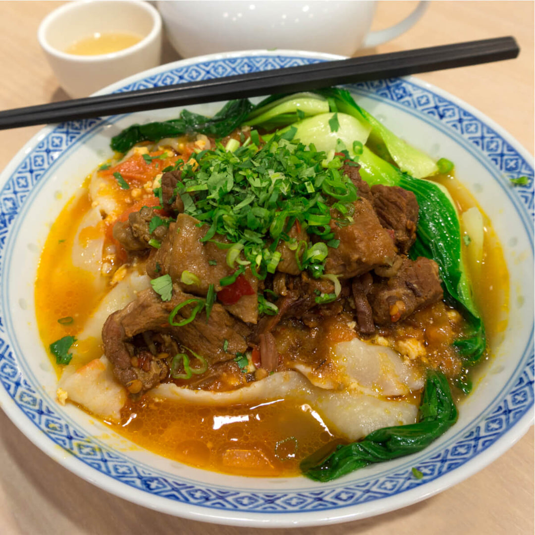 A bowl of TDG Knife Sliced Style Dao Xiao Mian Noodles with meat and vegetables in it.