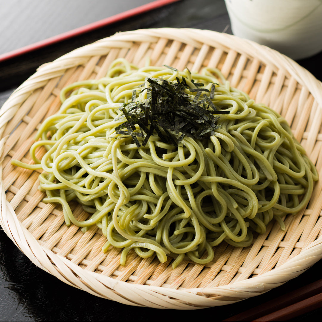 A bowl of Hakubaku Organic Cha Soba Green Tea Noodles on a table next to a cup of green tea.