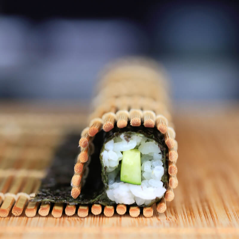 A Marufuji Makisu Sushi Bamboo Rolling Mat is sitting on a wooden table.