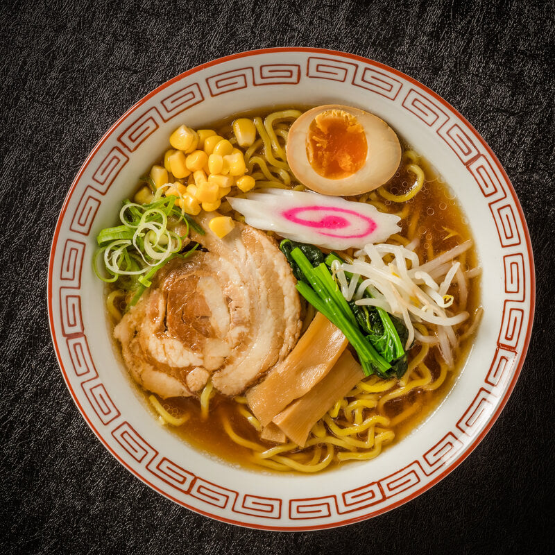 A bowl of traditional ramen with slices of pork, egg, corn, Momoya Menma Pickled Bamboo Shoots, and vegetables on top.